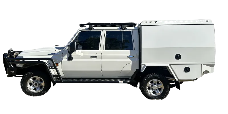 A white off-road pickup truck with a large white hardtop camper body attached, shown in a side profile on a plain white background. The truck is equipped with a black roof rack, black bull bar, black side steps, and black tires.