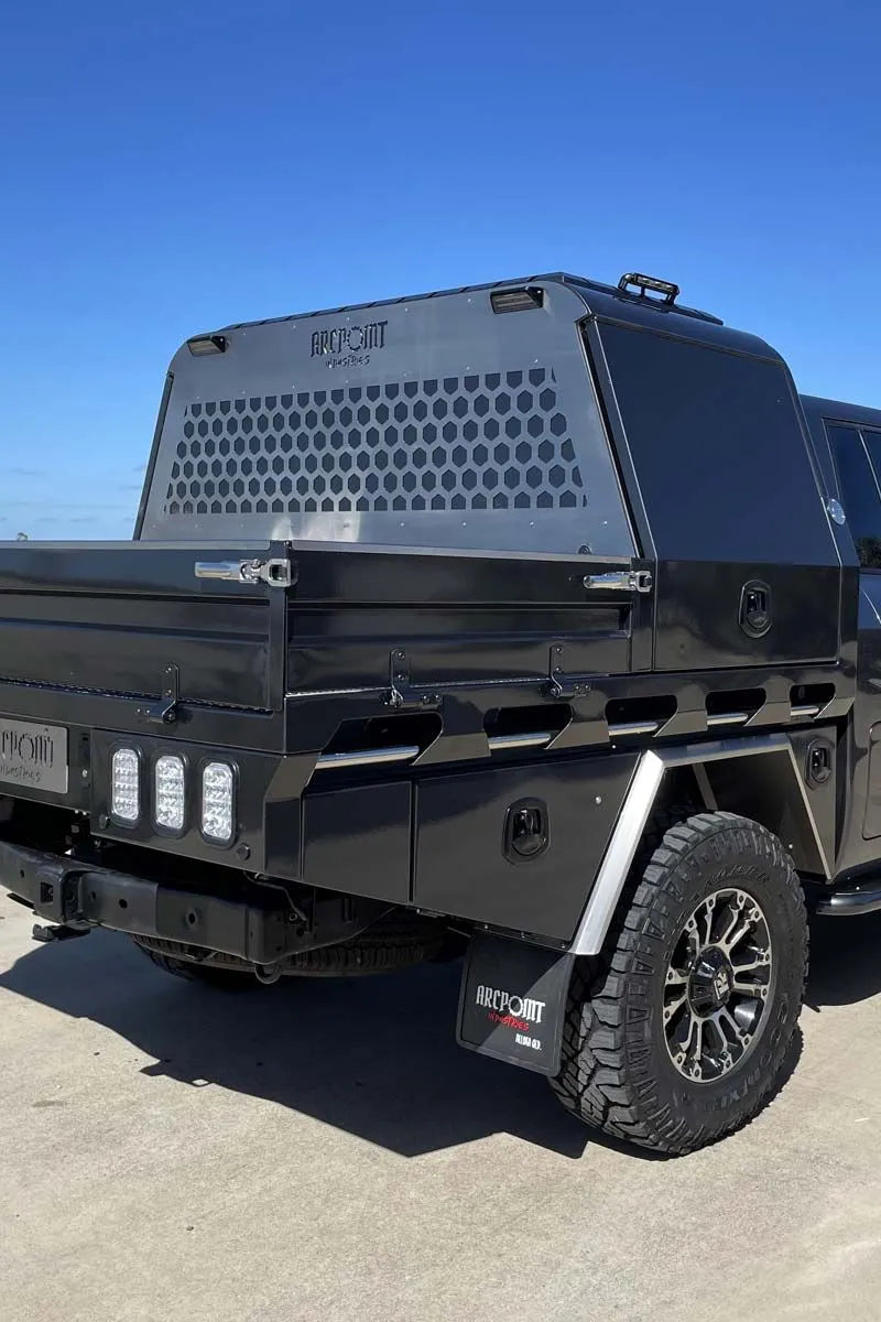 A black off-road truck with a large silver honeycomb-patterned canopy cover on the bed, photographed outdoors under a clear blue sky.