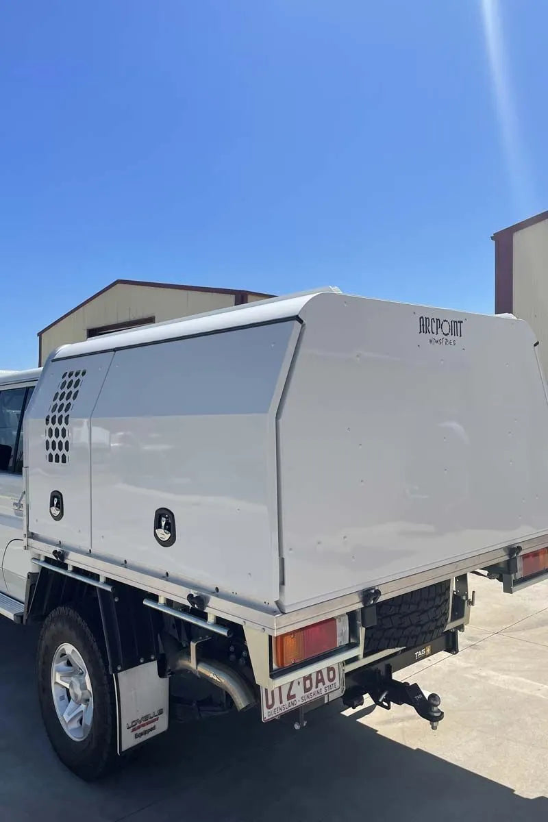 A white utility truck bed canopy with a hard side wall and rear ramp, photographed outdoors under a clear blue sky. The side panel shows the brand name 'BRISBANE AUTO' and a circular logo badge.